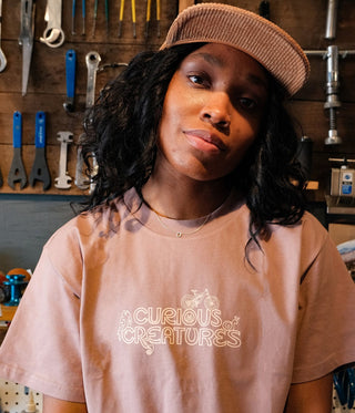 Dee hanging out in the bike shop with a brown corduroy hat and pink curious creatures printed tee