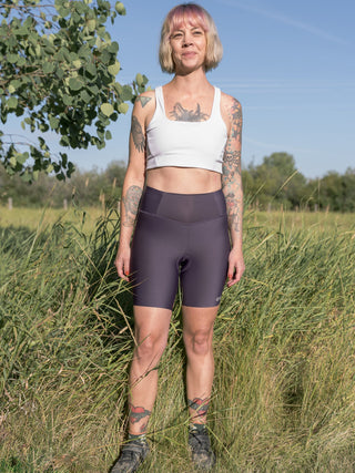 Holly stands next to an open field in Bozeman Montana wearing purple padded bike shorts