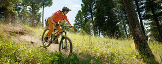 Lila speeds down a bright meadows of green on her bike amongst Montana pines