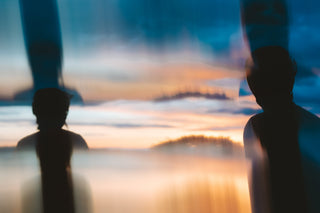 Silhouetted figures with bike helmets looking out to softly blurred sunset landscape with blue sky, warm orange light, and reflective glass.