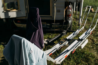 A light blue pocket tee with eyes logo and purple chamois hang to dry on a bike rack on the back of a Truck Camper at camp