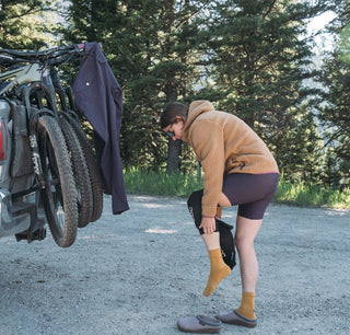 Rachel pulls on her bike knee pads before putting on her purple pants at a Montana trailhead 