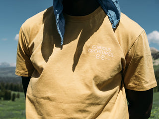 Closeup of the Curious Creatures logo on the front of the Faded Mustard Tee