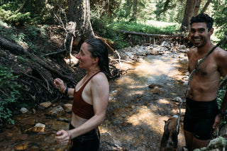 Hannah and Pasha laugh in the frigid creek wearing nothing but their chamois after a dusty ride up red cub in Montana
