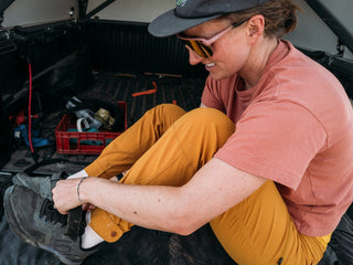 Hannah in the back of her pick up ties her shoes before a mountain bike ride in her stretchy buckthorn brown pants