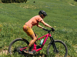 Hillary cuts across a Montana meadow on her bright pink Juliana and color coordinated Aragon Pocket T and short shorts