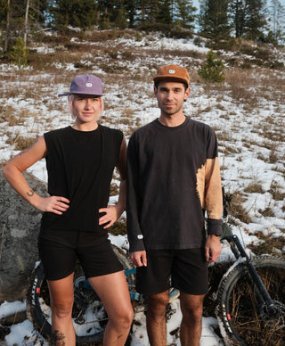 Sophie and Pasha pose on a snowy Montana trail in their all black clothes with a bike in the background